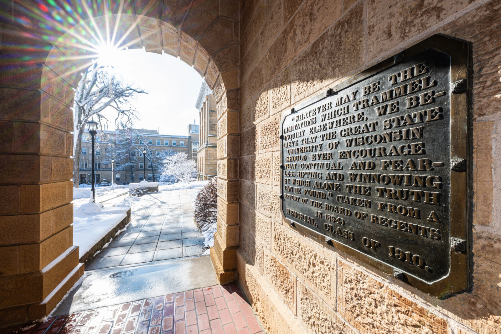 The winter-morning sunlight shines upon a close-up view of the letters on the "Sifting and Winnowing" plaque, mounted in the arched-portico of Bascom Hall at the University of Wisconsin–Madison. The streaked and blurred photograph was made by zooming the camera lens during time exposure. (Photo by Jeff Miller / UW–Madison)
